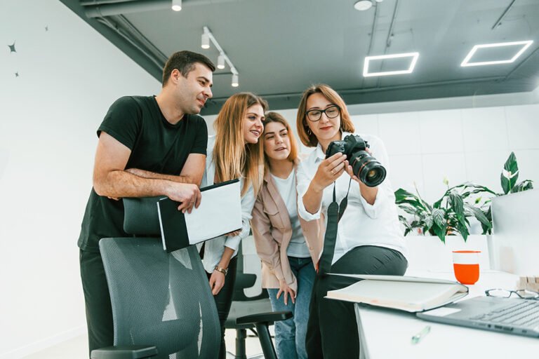 Group of business people in formal clothes indoors in the office looking at photos on the camera.